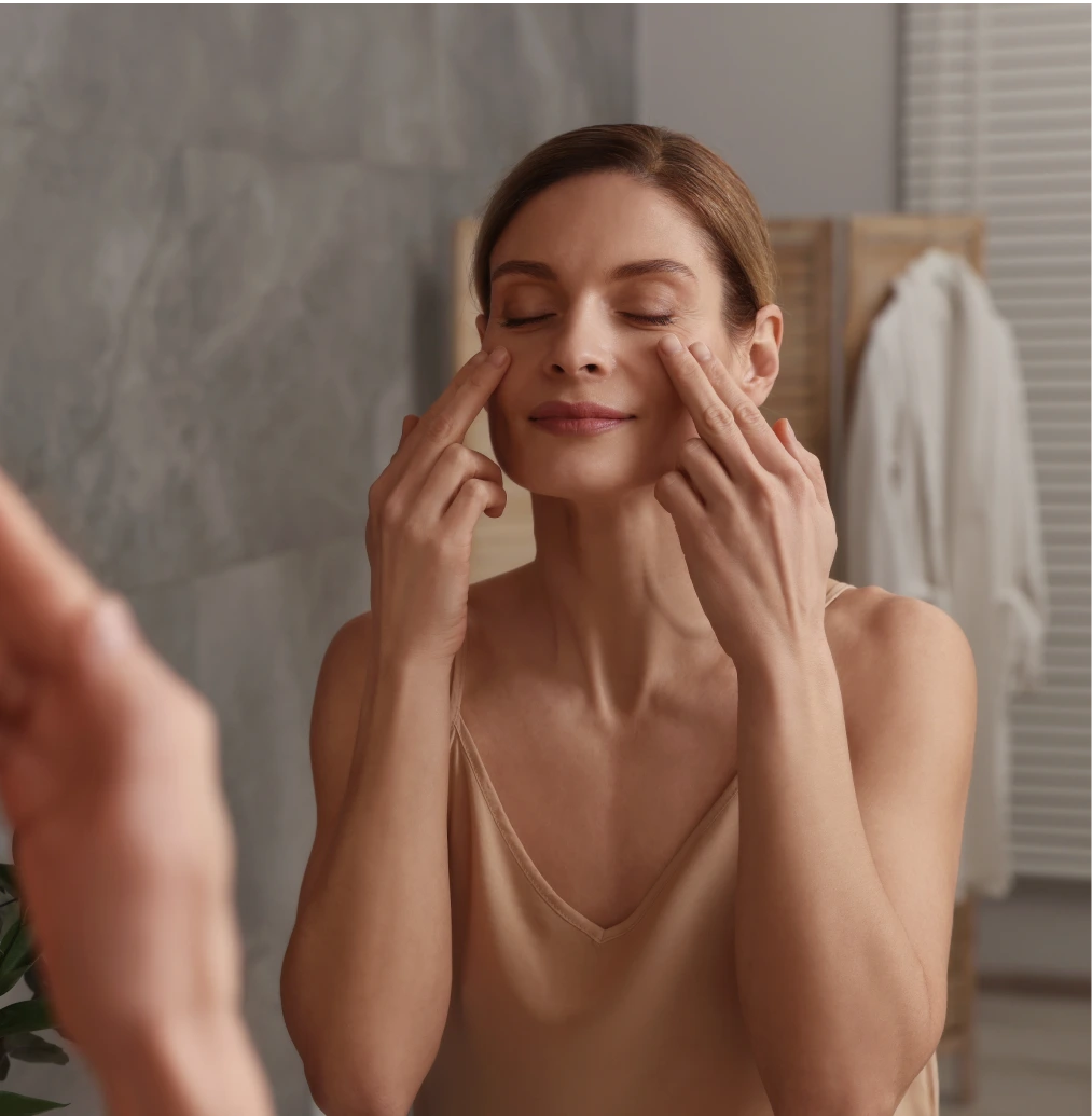 Woman applying skincare product to her cheeks in a bathroom mirror